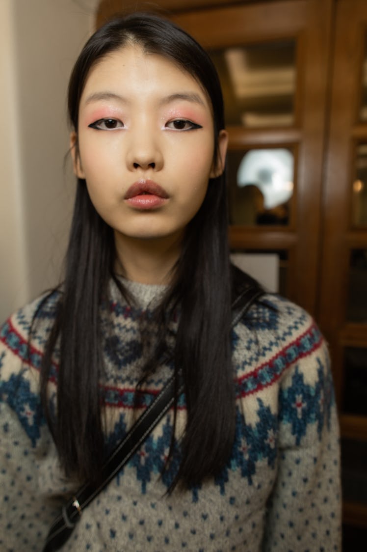 A close-up portrait of a model in a blue-beige-red sweater backstage at Richard Quinn‘s fall collect...