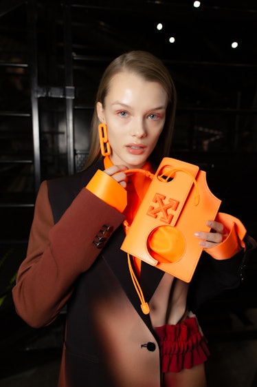 A model in a brown-black coat, orange earrings and an orange bag backstage at Off-White