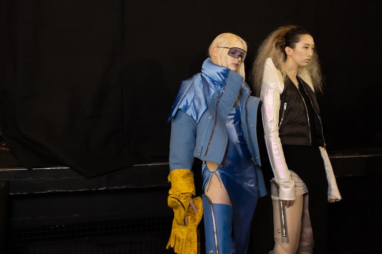 A model in a blue jacket and boots and a model in a black-white jacket backstage at the Rick Owens f...