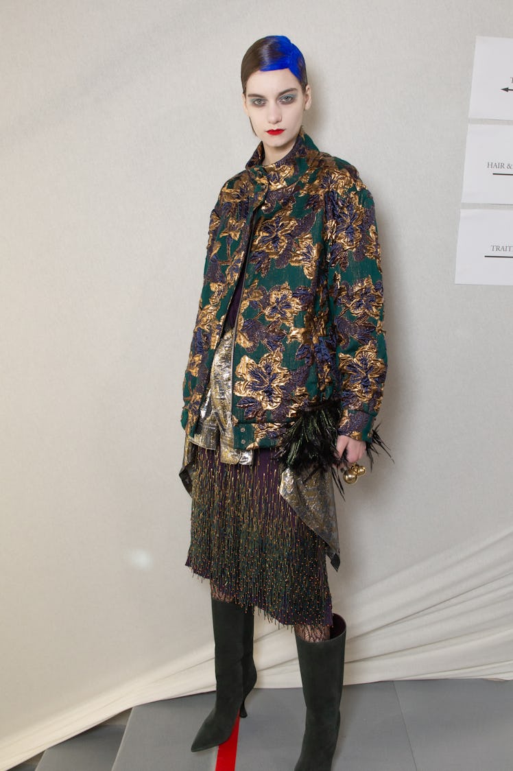 A female model posing while wearing a green jacket with flower drawings and a brown dress paired wit...