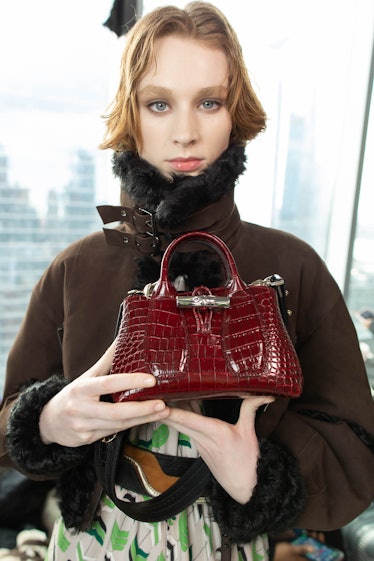 A female model holding a red bag while holding a brown jacket