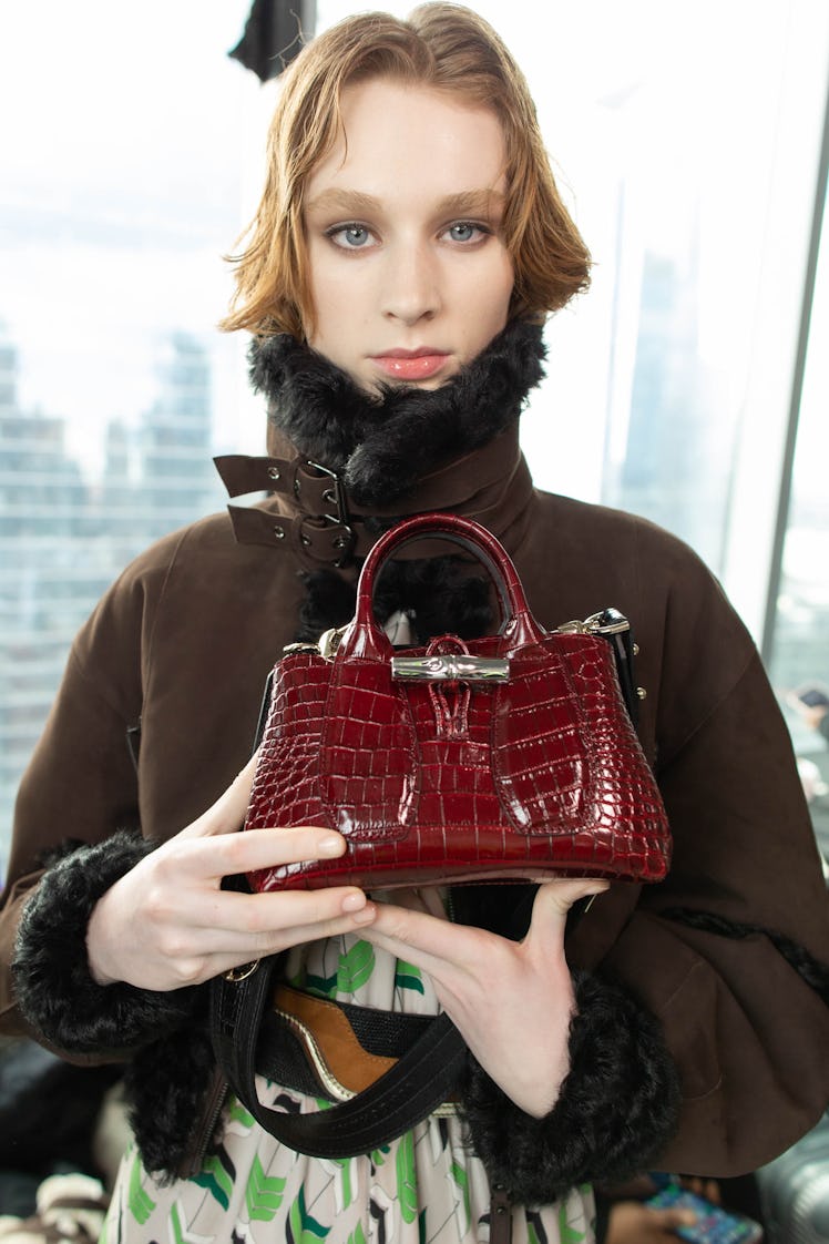 A female model holding a red bag while holding a brown jacket