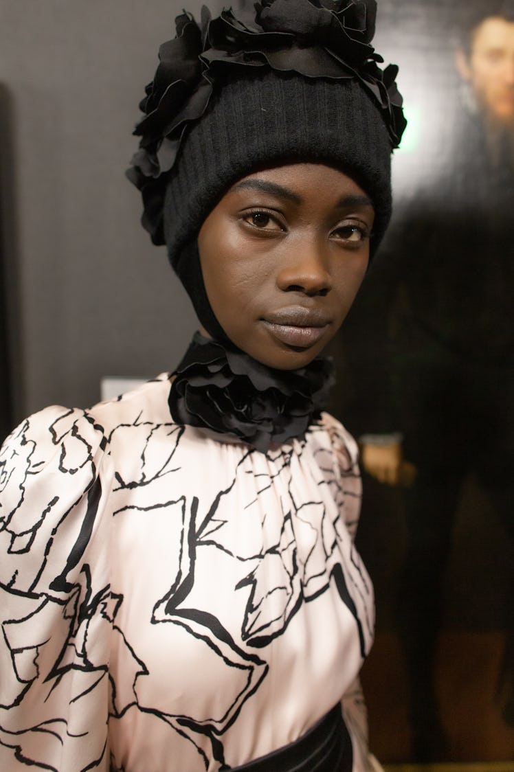 Model in a baby pink dress with black details, topped with a black beanie with black petals on top 