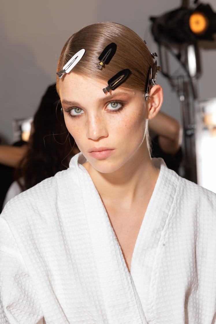 A female model sitting in backstage while wearing a white robe with hairclips on her sleek hair