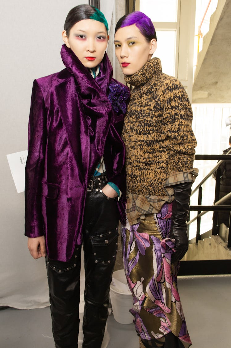 Two female models posing while wearing purple silk coats and brown sweaters