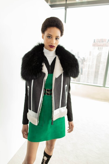A female model posing for a photo while wearing a green dress and a black and white jacket