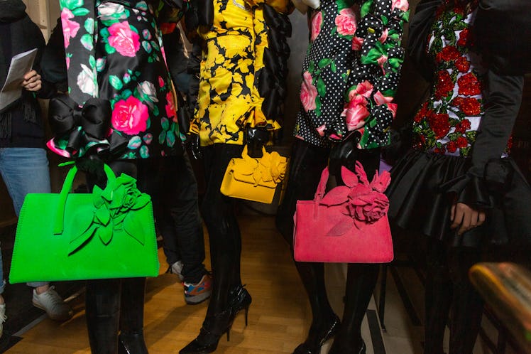 Four models standing in a row wearing floral dresses and bags backstage at Richard Quinn‘s fall coll...