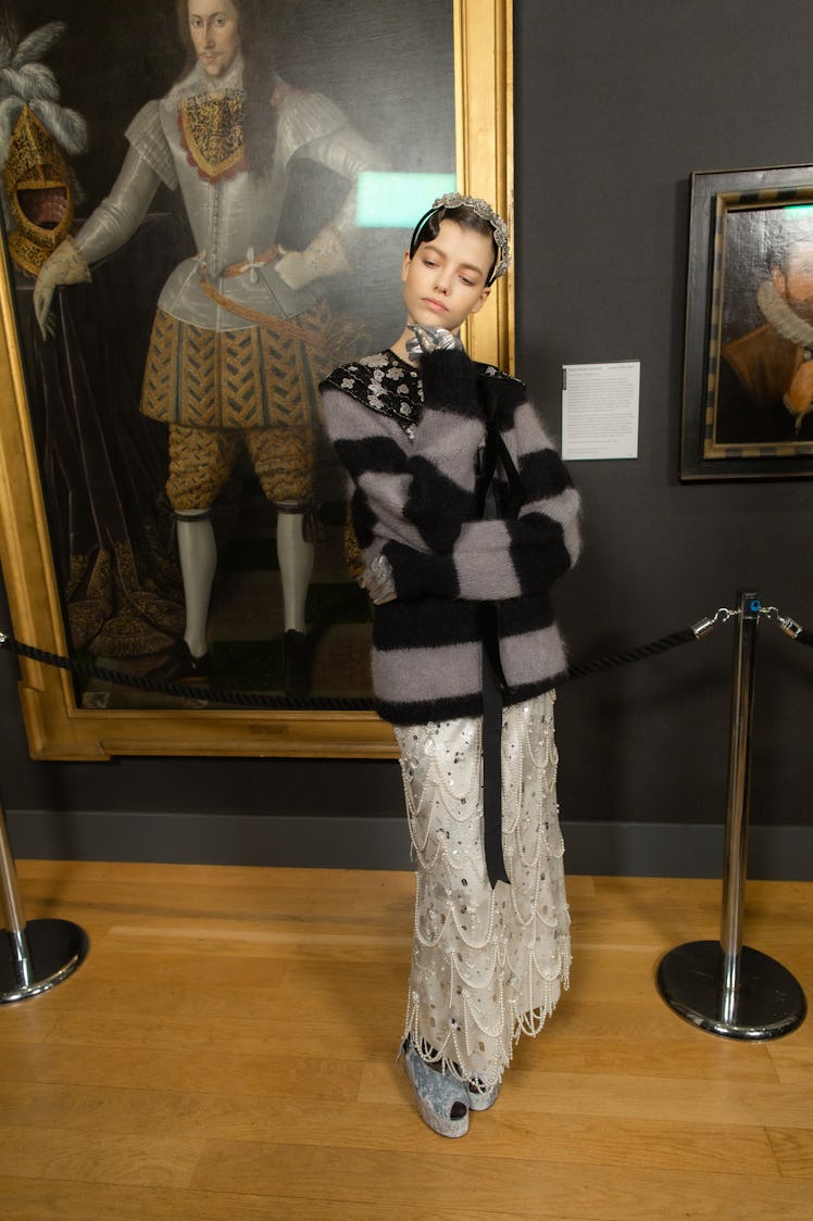 Model posing while wearing a sweater, a long skirt covered with pearls, and silver gloves