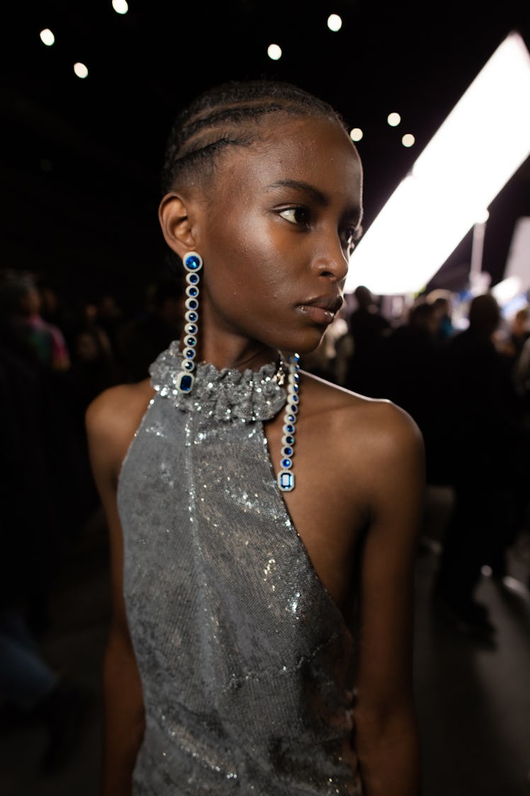 A model in a silver sequin dress and silver-blue earrings backstage at Off-White