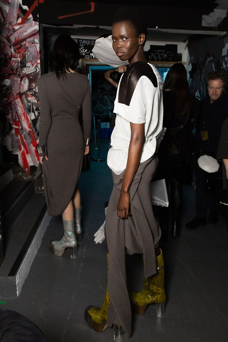 A model in a black-white shirt and grey trousers backstage at the Rick Owens fashion show
