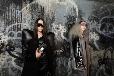 A model in a black jacket and a model in a grey-black jacket backstage at the Rick Owens fashion sho...