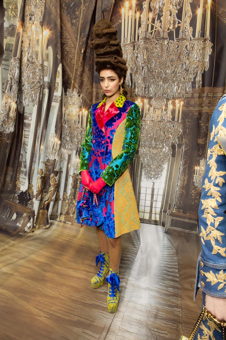 A model in a multi-colored patchwork floral coat and yellow-blue boots backstage at the Moschino Fal...