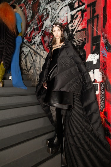 A model in a black dress and oversized black puffer jacket backstage at the Rick Owens fashion show
