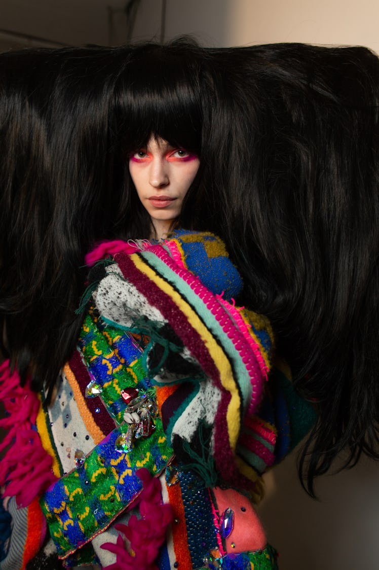 A model with a black oversized wig in a multi-colored dress backstage at the Matty Bovan fashion sho...
