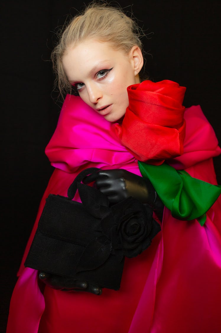A model wearing a pink cape with an oversized red rose, black gloves and a black bag at Richard Quin...