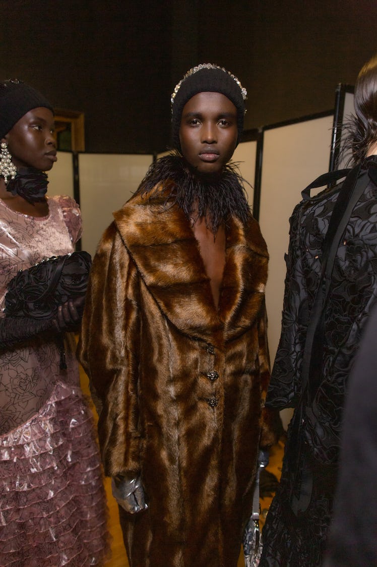 Model standing in queue and wearing a brown fur coat and feather collar