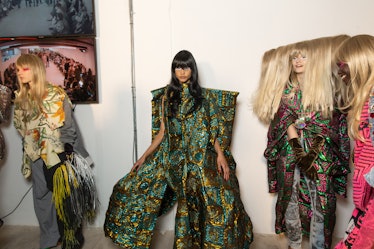 Three models in multi-colored multi-patterned asymmetric dresses backstage at the Matty Bovan fashio...