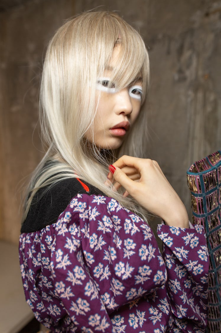 A model in a purple-white floral top and white eyeshadow backstage at the Matty Bovan fashion show