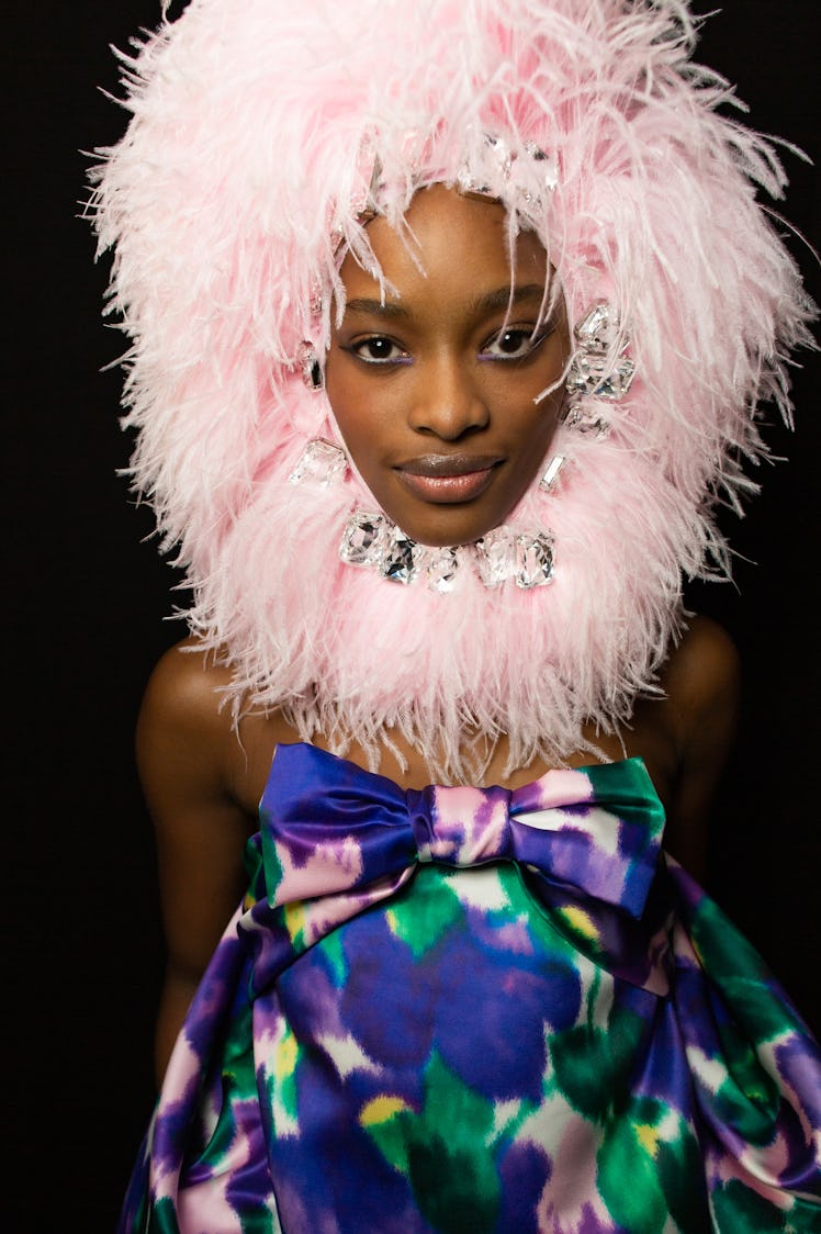 A model wearing a purple-green-pink satin dress with bow and a pink feather hat at Richard Quinn‘s f...