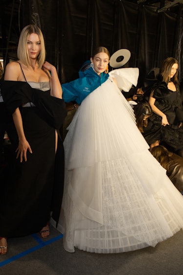 Karlie Kloss in a black dress with grey bustier and Gigi Hadid in a white tulle dress backstage at O...