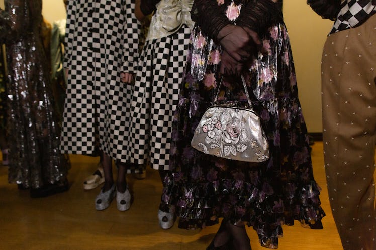 Model holding an embroidered bag, while two models beside her are wearing checkered dresses
