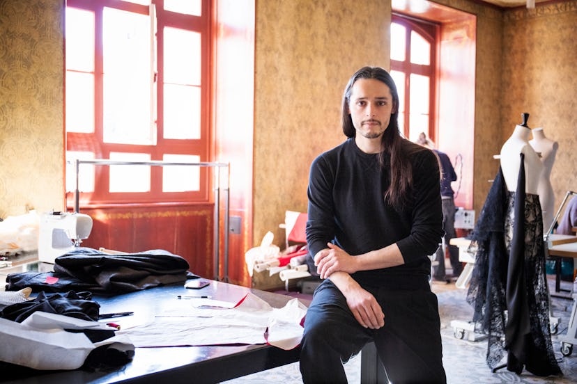 Olivier Theyskens in a black shirt and black trousers sitting on the edge of a table in his studio