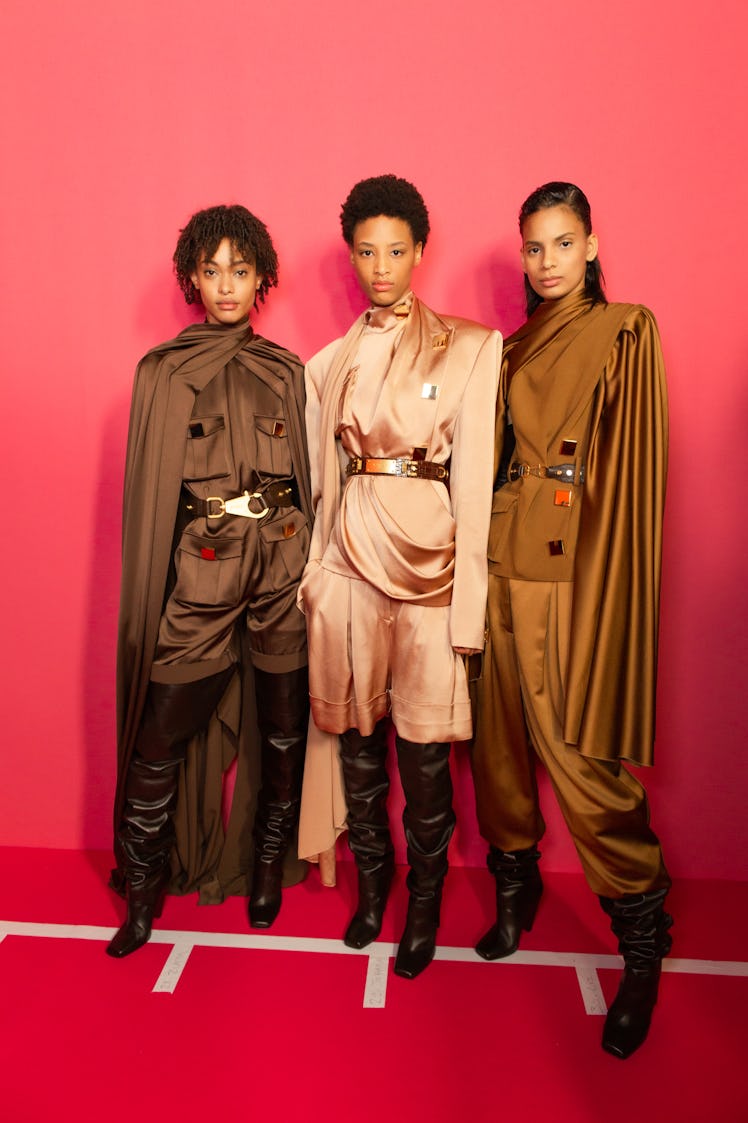 Three models in a brown suit, peach suit and bronze suit backstage at Balmain Fall 2020