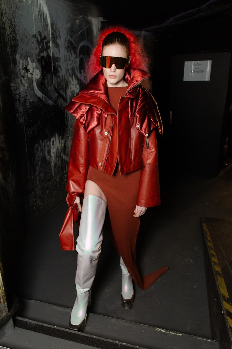 A model in a red dress and jacket and white boots backstage at the Rick Owens fashion show