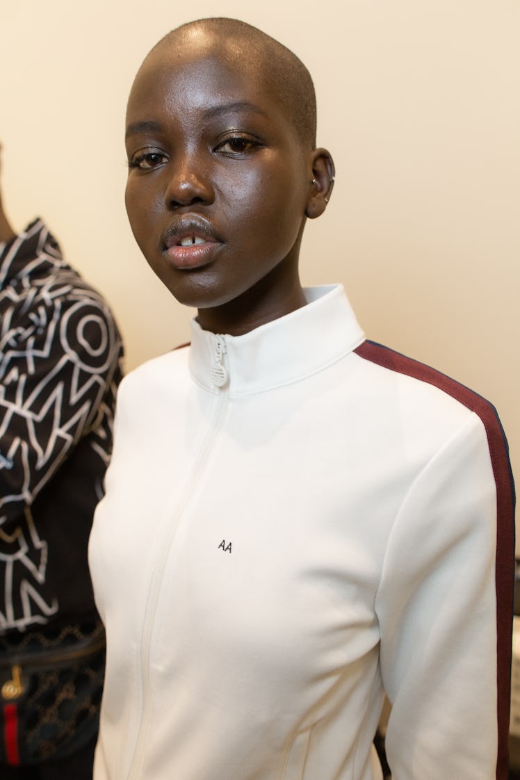 A bald model posing for a photo in a white tracksuit top