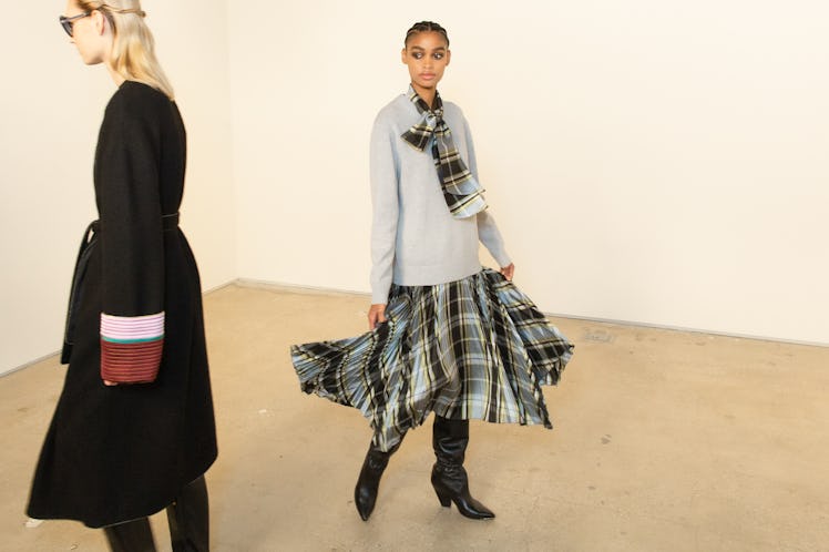 A model in a grey shirt and plaid dress posing for a photo at the Tory Burch FW20 during New York Fa...