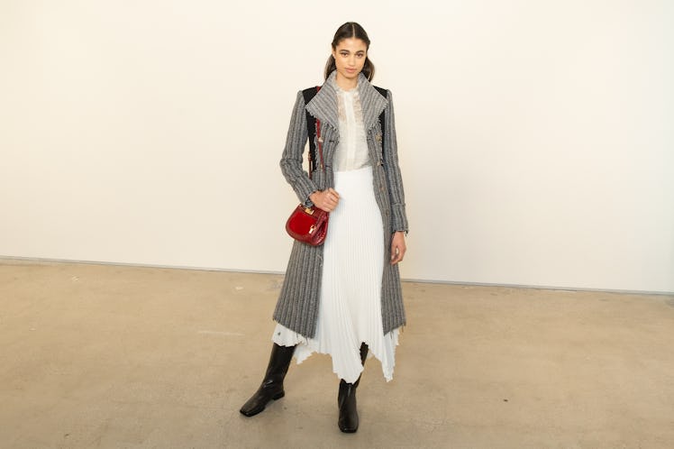 A female model posing for a photo in a grey coat and white dress at the Tory Burch FW20 during New Y...