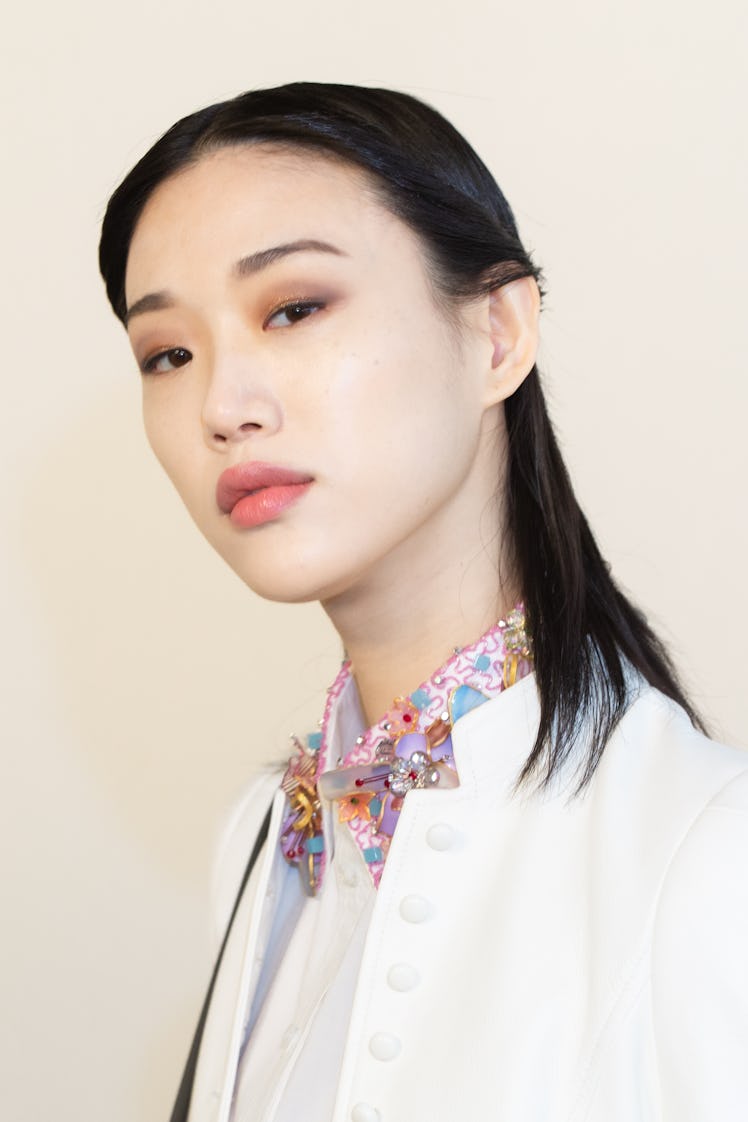 A black-haired female model posing for a photo in a white blazer 