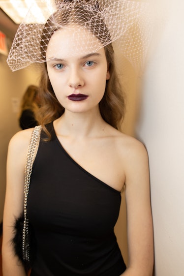 A female model posing while wearing a black dress and a white veil on her head