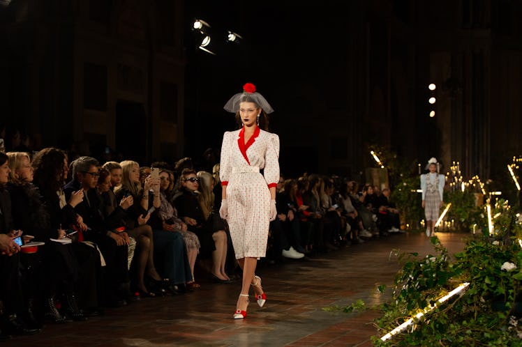 A female model walking a runway while wearing a white and red dress