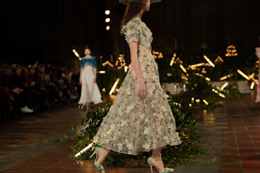 A female model walking a runway while wearing a green floral gown