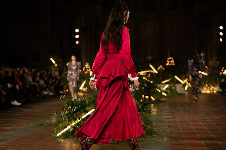 A female model walking a runway while wearing a red dress