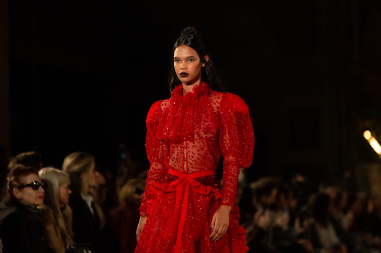 A female model walking a runway while wearing a red gown