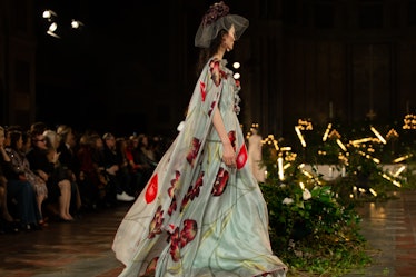 A female model walking while wearing a light blue gown with red drawings