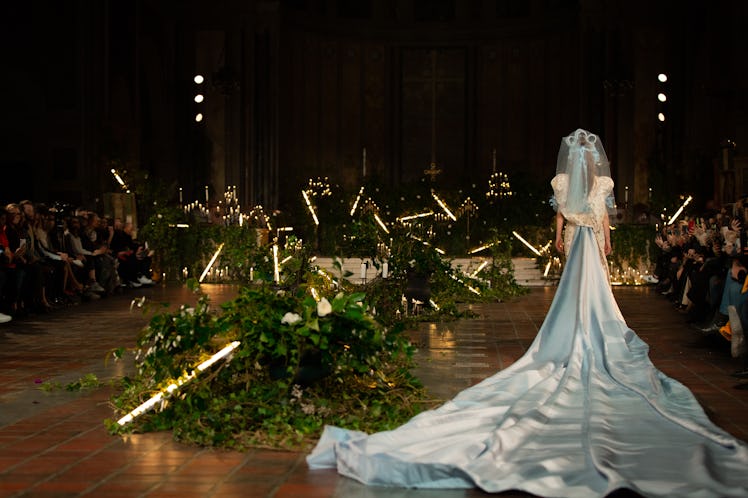A female model walking a runway while wearing a light blue wedding gown