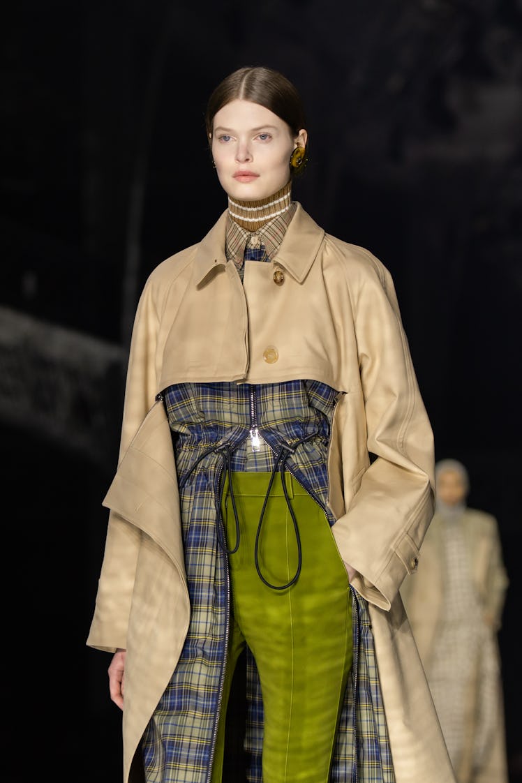 A model wearing a blue-green checked shirt, olive trousers and a beige coat at the Burberry Fall 202...