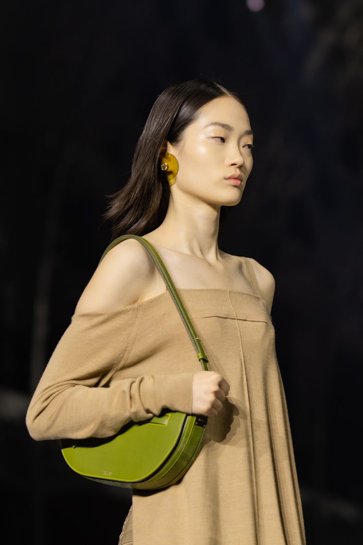 A model wearing a beige dress, olive bag and orange earrings at the Burberry Fall 2020 show