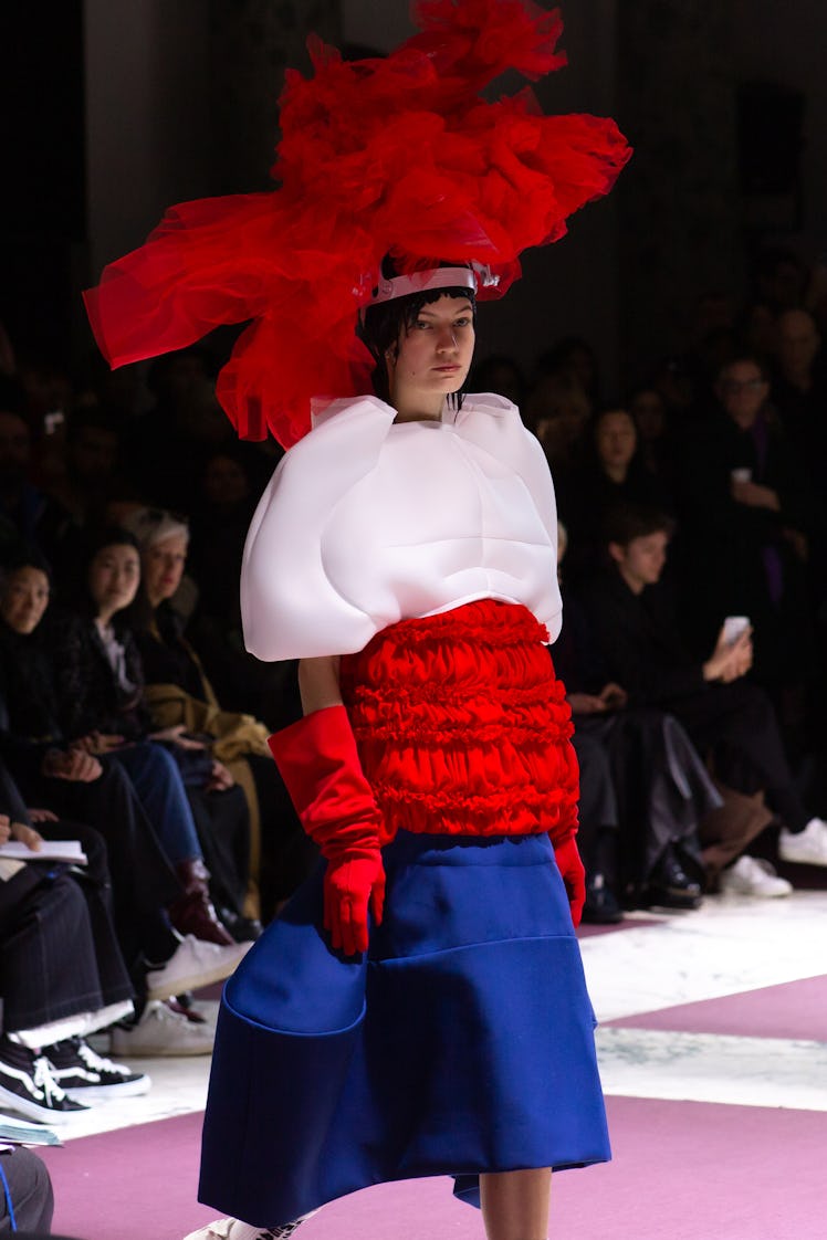 A model on Comme Des Garcons' runway in a puffy white blouse, red gloves, a red and blue skirt, and ...