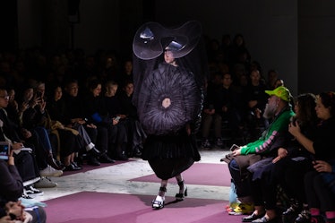 A model on Comme Des Garcons' runway in a black dress with a black 3D circle in the middle and a lar...