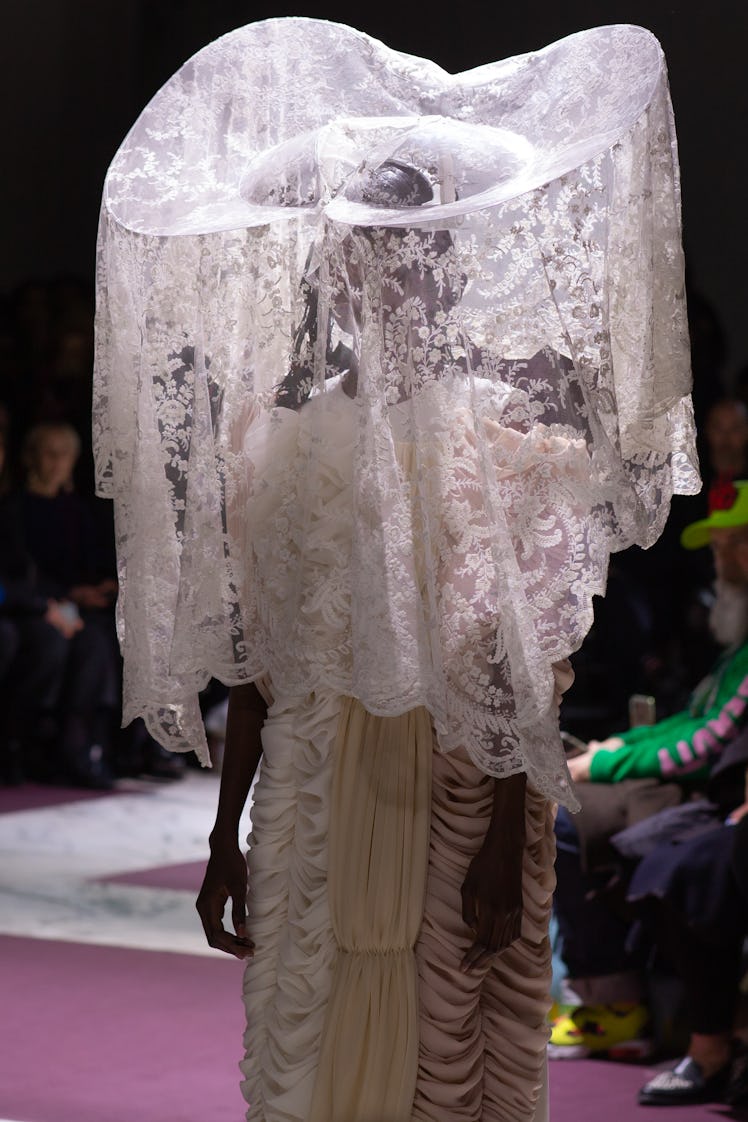 A model on Comme Des Garcons' fall 2020 runway in a long white dress and large white lace headpiece ...