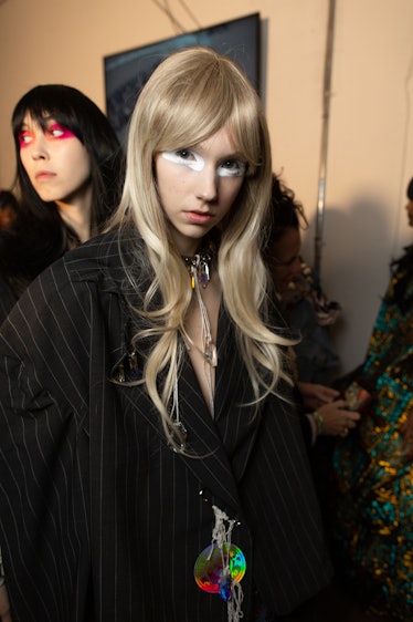 A model in a black pinstripe coat and white eyeshadow backstage at the Matty Bovan fashion show