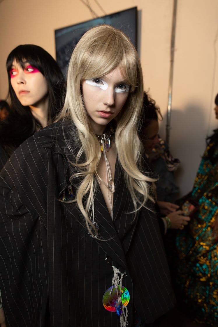 A model in a black pinstripe coat and white eyeshadow backstage at the Matty Bovan fashion show