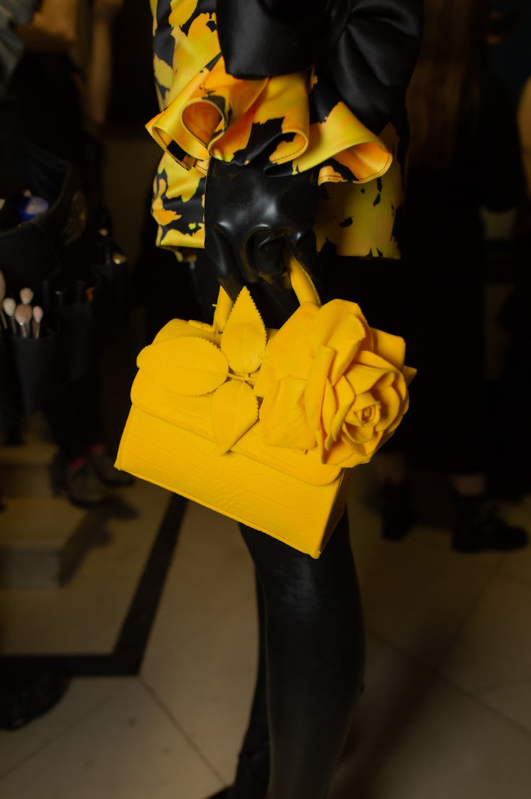 A close-up of a model wearing a yellow bag with an oversized yellow rose at Richard Quinn‘s fall col...