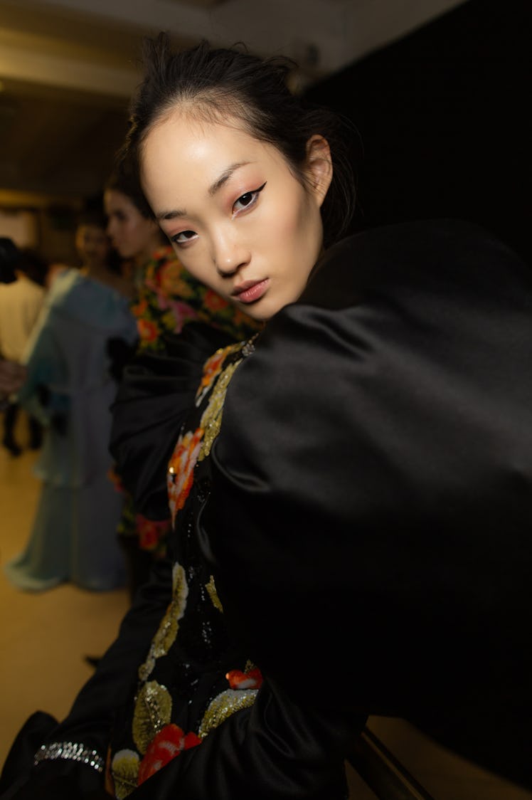 A close-up portrait of a model in a black dress backstage at Richard Quinn‘s fall collection
