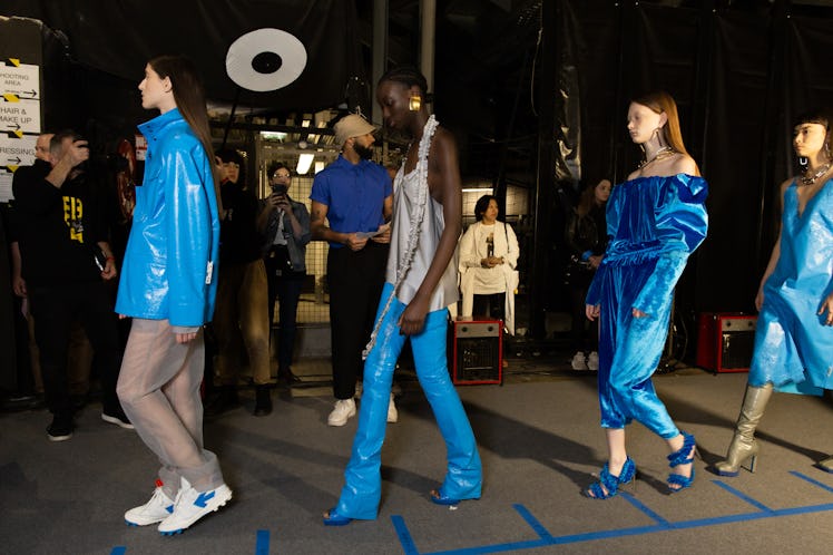 Four models in blue-grey-silver outfits walking in a line backstage at Off-White