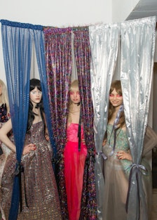 Three models posing in a silver, pink and green dress Backstage at the Matty Bovan fashion show
